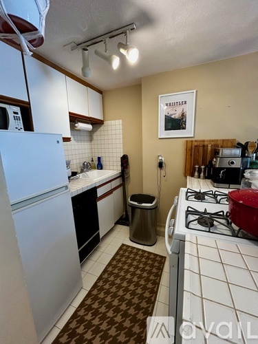 A kitchen with a white fridge, black stove and a brown patterned rug.