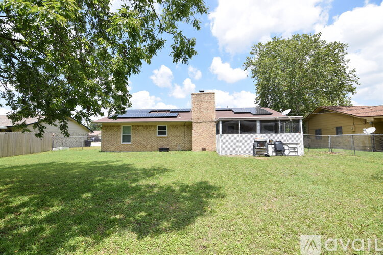 A house with a brown roof and a white fence is surrounded by a grassy yard.