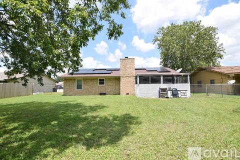 A house with a brown roof and a white fence is surrounded by a grassy yard.