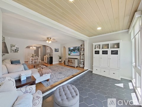 A spacious living room with a white couch and a grey ottoman.