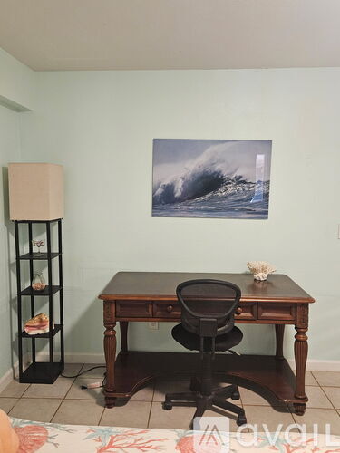A wooden desk with a black chair and a painting of a wave on the wall.