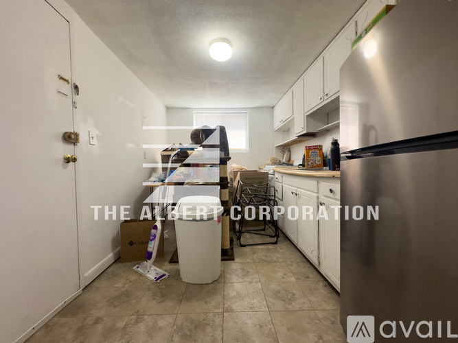 A kitchen with a refrigerator, cabinets, and a trash can.