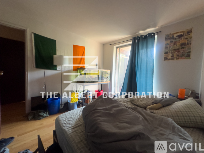 A bedroom with a bed, a window with curtains, and a lamp on a shelf.
