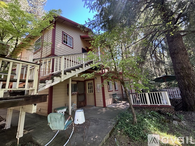 A house with a red trim and a balcony is surrounded by trees.