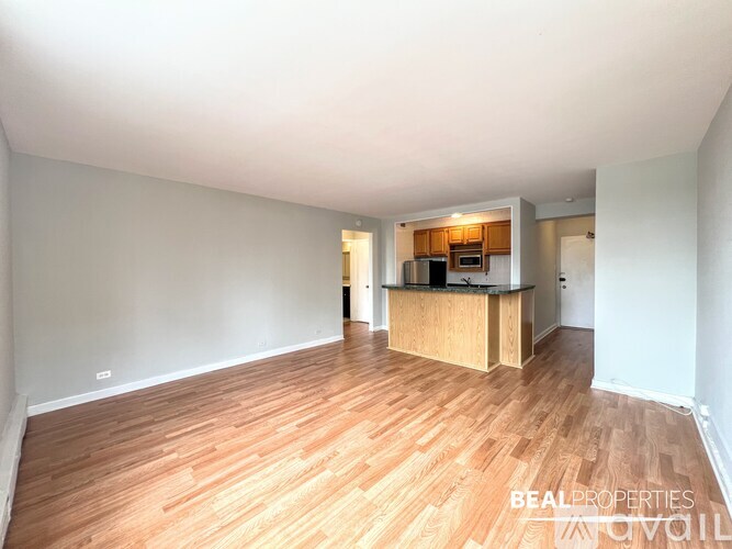 A spacious room with wooden flooring and a kitchen area in the background.