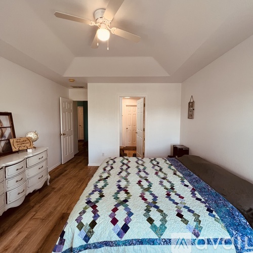 A bedroom with a bed covered in a quilted blanket and a ceiling fan.