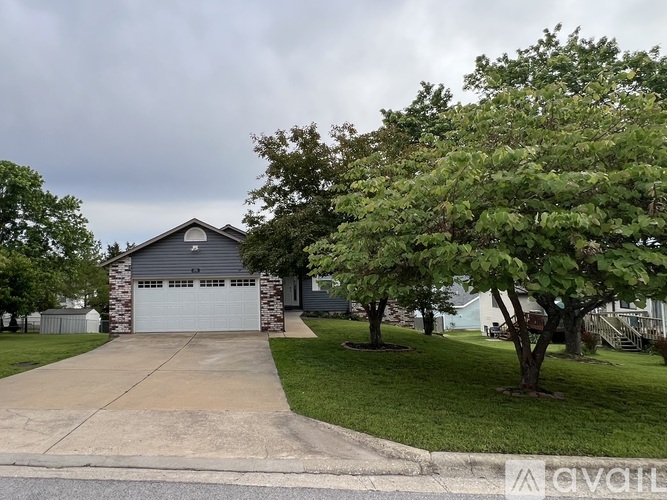 A house with a grey roof and a white garage door is surrounded by trees.