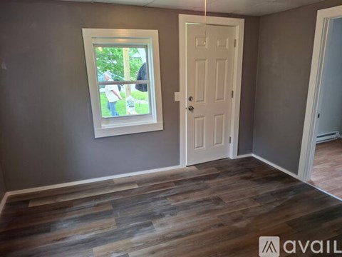 A room with a white door and a window with a view of trees and people outside.