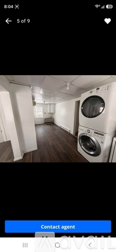 A washing machine is placed in a room with white walls and wooden flooring.