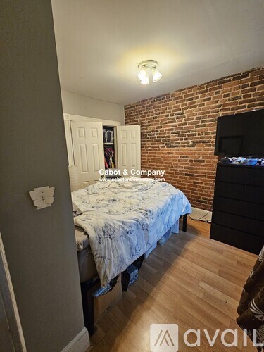 A bedroom with a bed, dresser, and a brick wall.