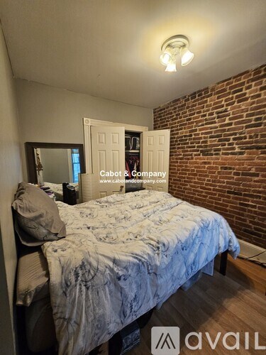 A bedroom with a bed, a mirror, and a brick wall.