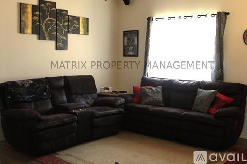 A living room with a black leather couch and a matching chair, a framed picture on the wall, and a window with curtains.
