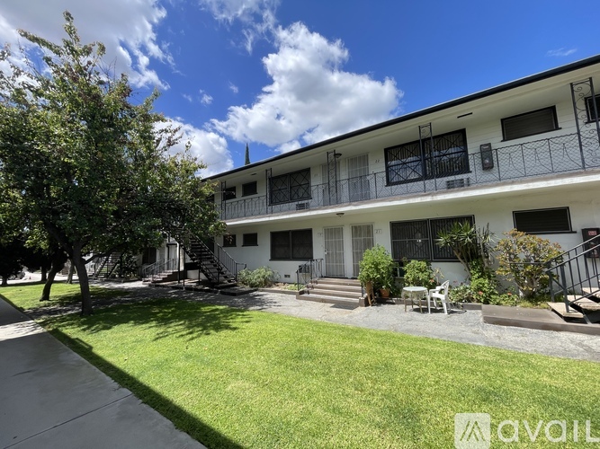 A sunny day at a white two-story apartment building with a tree in the front yard.