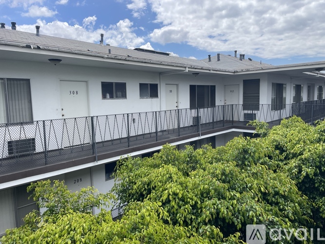Apartment complex with balconies and trees in front.