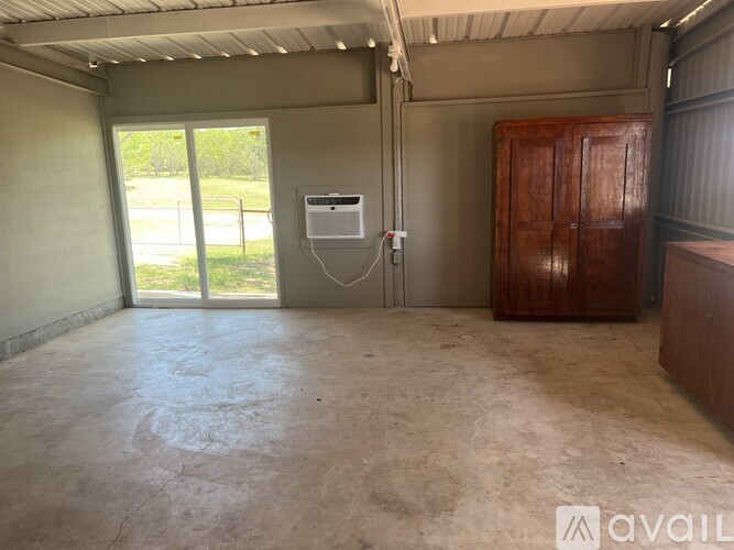 A room with a concrete floor and a window with a view of a fence and trees.