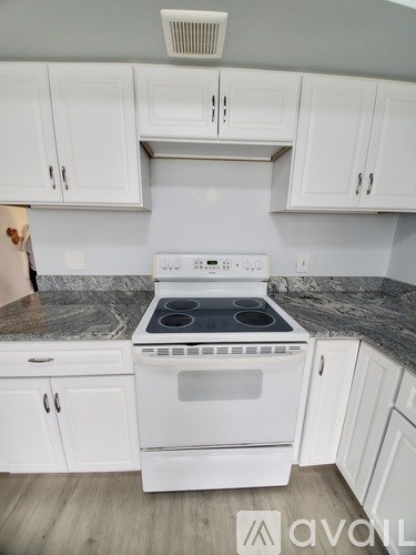 A white stove top oven with four burners and a white oven door sits on a granite countertop in a kitchen with white cabinets.