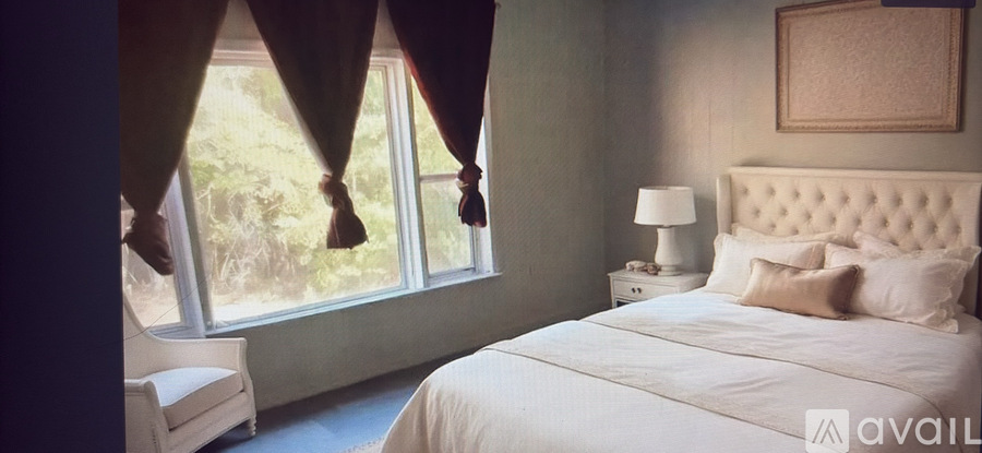 A bedroom with a large bed and a window with curtains.