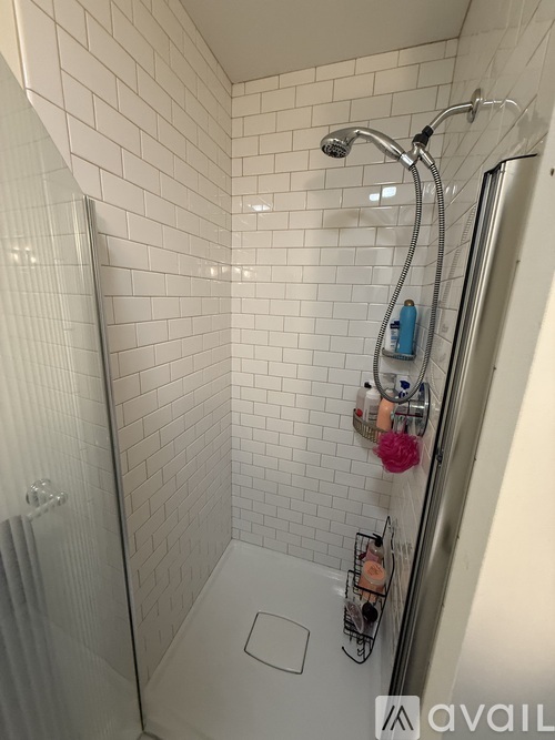 A white tiled shower with a shower head and a hose.