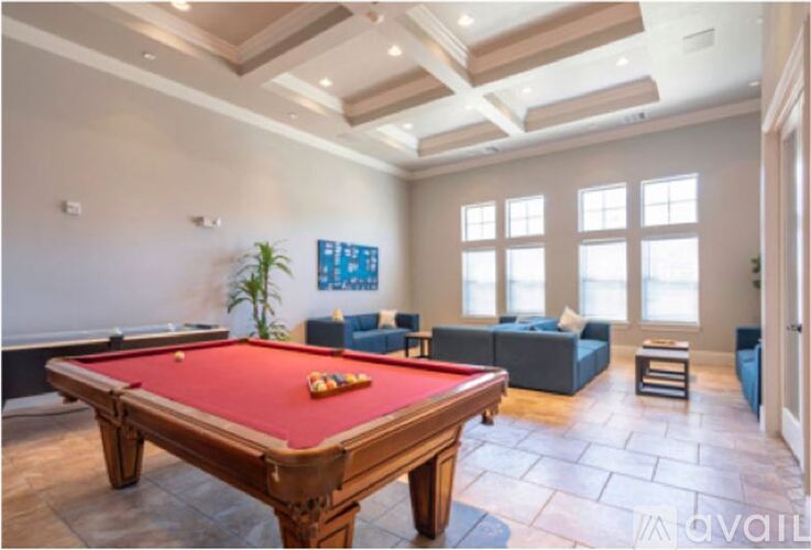 A pool table is in the middle of a room with a couch and a plant.