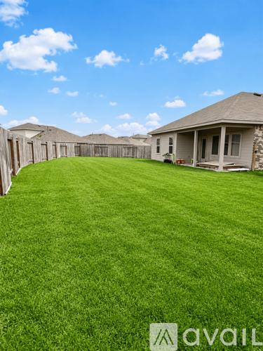 A grassy backyard with a house and a fence.
