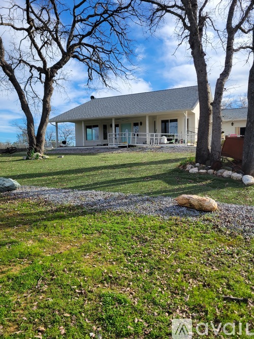 A house with a grey roof and a porch surrounded by trees and grass.