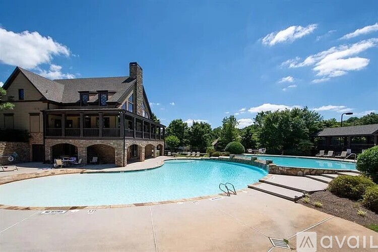 A large swimming pool in front of a house with a stone chimney.
