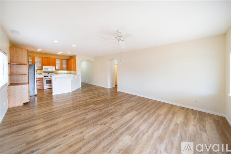 A spacious room with wooden flooring and a kitchen area in the background.