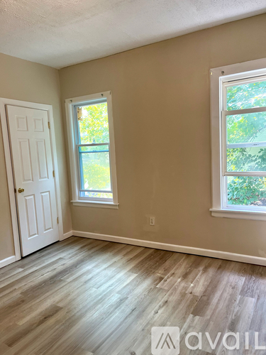 A room with a white door and a window with a view of trees.