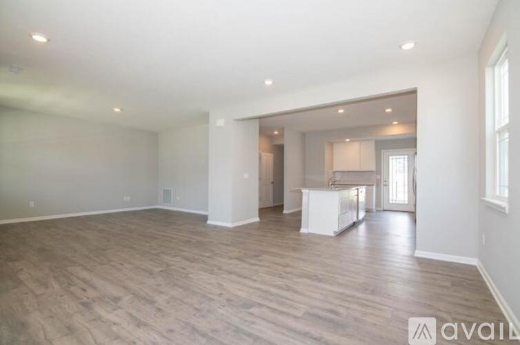A spacious room with wooden flooring and a kitchen area in the background.
