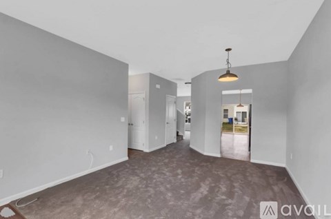 A spacious room with a grey floor and walls, a hanging light fixture, and a doorway leading to another room.