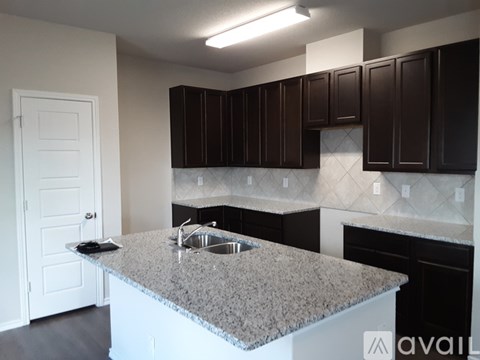 A kitchen with a granite countertop and dark brown cabinets.