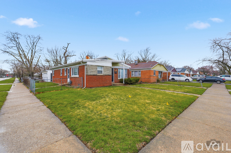 A house with a red brick exterior is surrounded by a grassy lawn and a sidewalk.