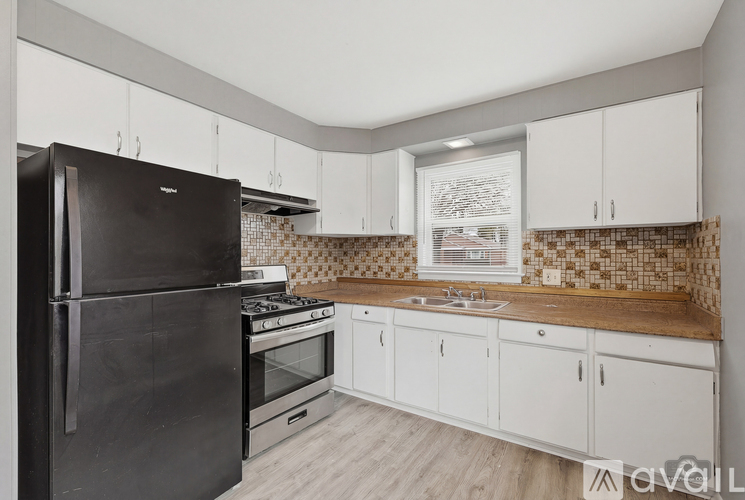 A kitchen with a black fridge, white cabinets, and a brown countertop.