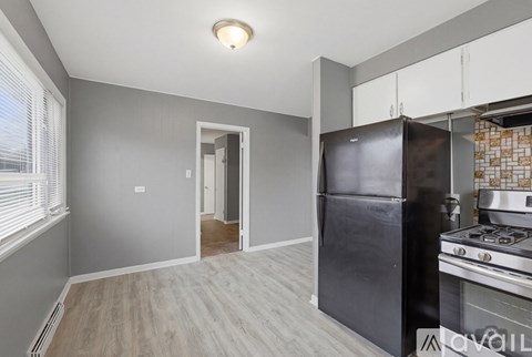 A kitchen with a black fridge and stove next to a hallway.
