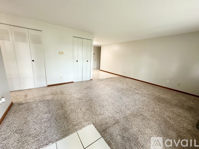 A room with carpeted floor and white walls with a row of white cupboards.