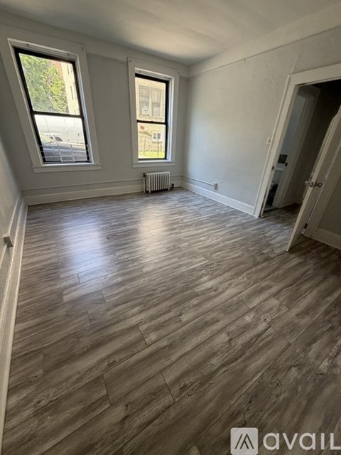 A room with wooden flooring and two windows.