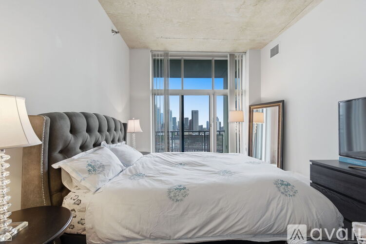 A bedroom with a large bed and a city view through the window.