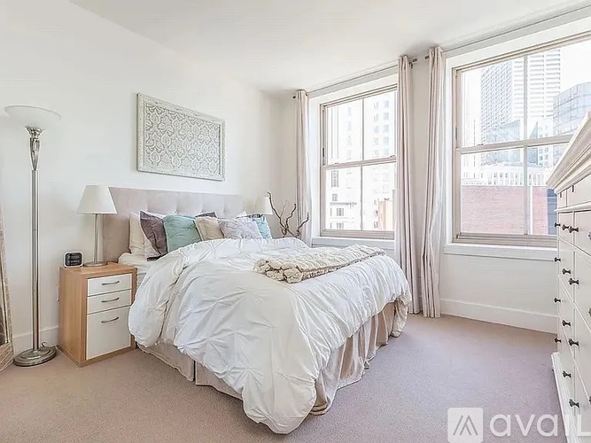 A bedroom with a large bed, a nightstand with a lamp, and a framed picture on the wall.