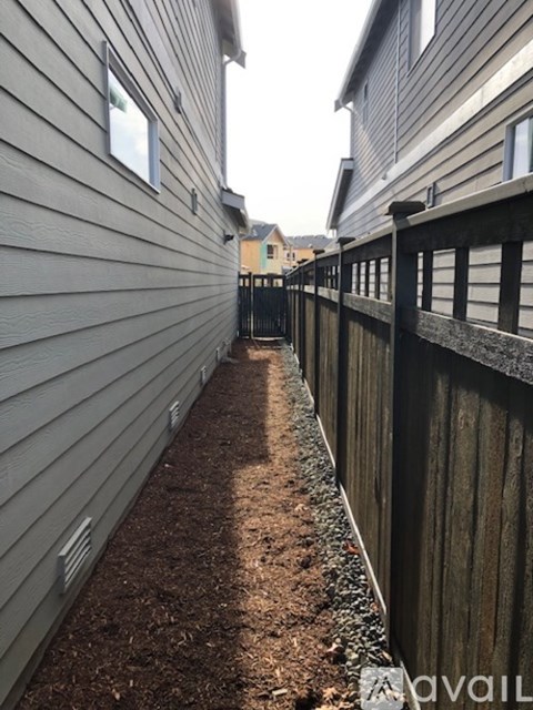 A narrow alley with a wooden fence on one side and a grey siding building on the other.