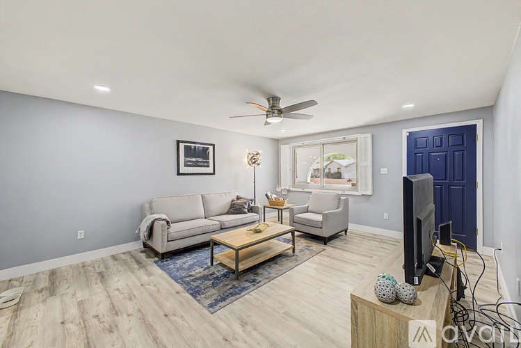 A living room with a grey couch, a wooden coffee table, a flat screen TV and a ceiling fan.