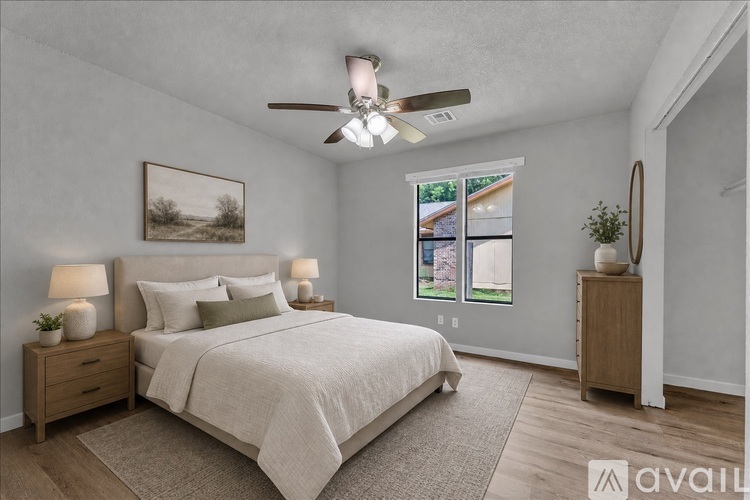 A bedroom with a large bed, a ceiling fan, and a window with a view of a house.