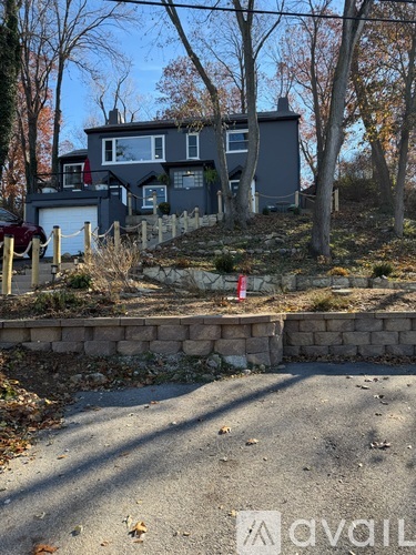 A house with a grey exterior is surrounded by trees and a stone wall.