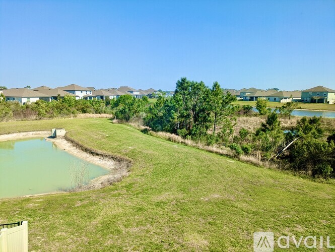 A grassy field with a pond and a row of houses in the distance.