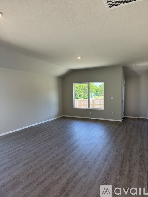 A room with wooden flooring and a window showing greenery outside.
