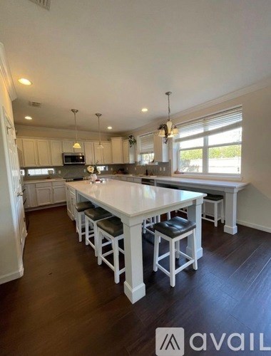 A kitchen with white cabinets and a long island with stools.