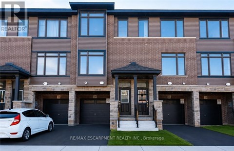A white car is parked in front of a building with a sign that reads RE/MAX Escarpment Realty Inc., Brokerage.