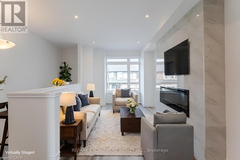 A living room with a white sofa, a grey armchair, a coffee table, and a flat-screen TV mounted on the wall.