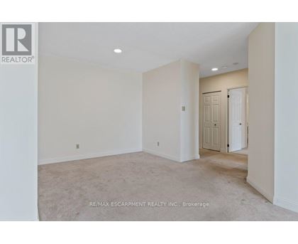 A spacious room with beige carpeting and white walls, with a door visible in the background.