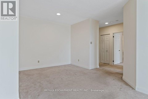 A spacious room with beige carpeting and white walls, with a door visible in the background.