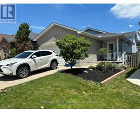 A white car is parked in front of a house with a tree and a flower bed.